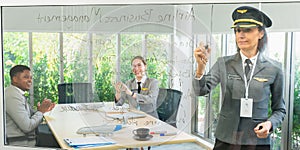 Businesswomen manager wear pilot hat, write on board in front of African man and cacuasian women cheering in meeting room.