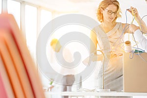 Businesswomen removing tangled cables from box at desk in new office with yellow lens flare in background