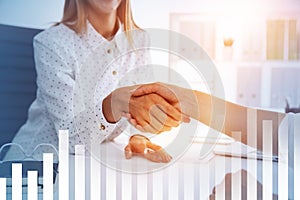 Businesswomen shaking hands in office, graphs