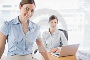 Businesswomen smiling at camera at their desk