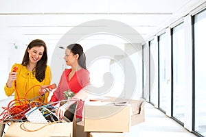 Businesswomen untangling cords while standing by cardboard boxes in new office