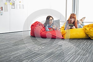 Businesswomen using digital tablets while relaxing on beanbag chairs in creative office