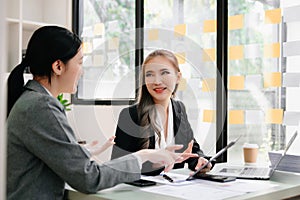 Businesswomen work and discuss their business plans. A Human employee explains and shows her colleague the results paper in office