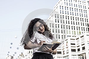 Businnes woman talking on the mobile phone with client and checks the schedule in her notebook