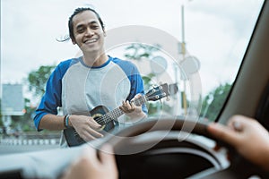 busker holding the ukulele is visible from the front of the windshield when the car photo