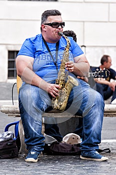 Fat busker playing sax seated on a bench