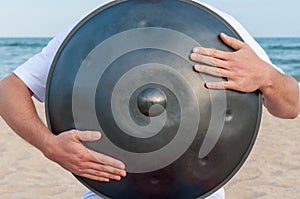 Busker on the sand beach and holding a handpan or hang with sea On Background. The Hang is traditional ethnic drum