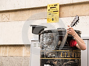 Busker singing and playing guitar inside a rubbish bin