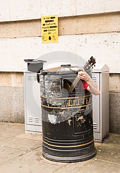 Busker singing and playing guitar inside a rubbish bin