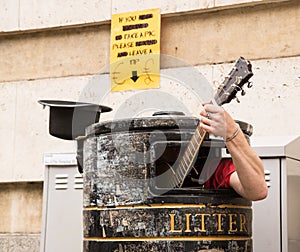 Busker singing and playing guitar inside a rubbish bin