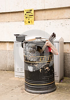 Busker singing and playing guitar inside a rubbish bin photo