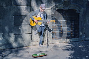 A busker street musician playing music with guitar on a city sidewalk photo