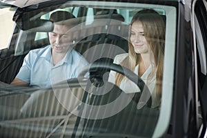 Bussines woman choosing car i car showroom. Salesperson sitting in car with customer and show desing