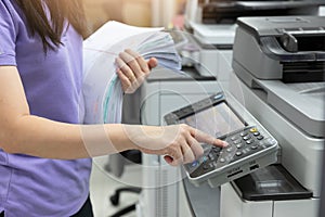 Bussinesswoman using copier machine to copy heap of paperwork in office