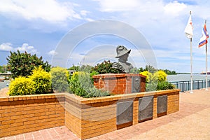 A bust statue of a Spanish explorer on the Savannah riverfront surrounded by red brick and lush green plants and yellow flowers