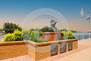 A bust statue of a Spanish explorer on the Savannah riverfront surrounded by red brick and lush green plants and yellow flowers