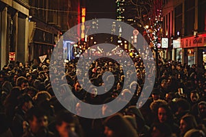 A bustling crowd of people walking down the street at night, filled with revelers and activity, A bustling crowd of revelers in photo
