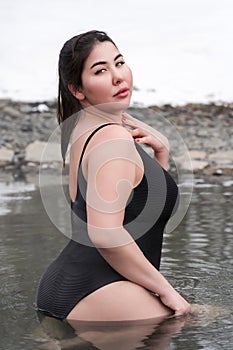 Busty curvy extended sizes young adult model in black bathing suit sitting in pool balneotherapy spa