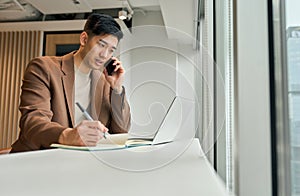 Busy Asian business man making phone call using laptop in office.