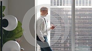 Busy business man standing in office holding cellphone using phone.