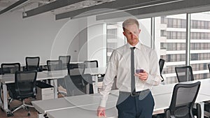 Busy business man standing in office holding cellphone using phone.