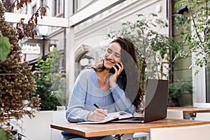 Busy business woman with laptop and phone is chatting and working remotely with colleagues. Cheerful girl with phone and