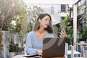Busy business woman with laptop and phone is chatting and working remotely with colleagues. Cheerful girl with phone and