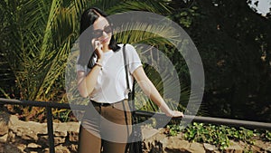 Busy business woman in sunglasses talking at mobile phone, teamwork conversation near exotic palm trees. Beautiful young