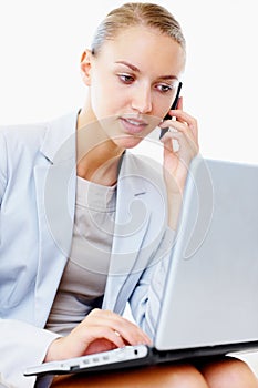 Busy business woman using cellphone and laptop. Pretty young business woman using a laptop and speaking on the cellphone