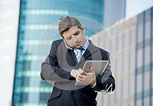 Busy businessman holding digital tablet and mobile phone overworked outdoors