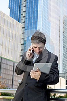 Busy businessman holding digital tablet and mobile phone overworked outdoors