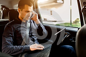 Busy businessman in a taxi. Multitasking concept. Passenger rides in the back seat, and works at the same time. Speaks