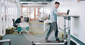Busy businessman walking on a treadmill desk while working on a laptop at work or in modern office workplace. Trendy