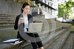 A busy businesswoman is sipping coffee and responding to messages on her phone on the stairs