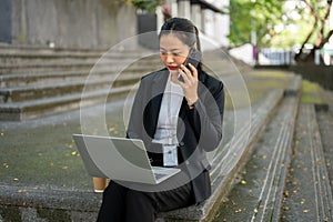 A busy businesswoman is talking on the phone while working on her laptop on the stairs in the city