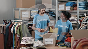 Busy caucasian male and female donation center workers working standing in warehouse and packing boxes with ordered