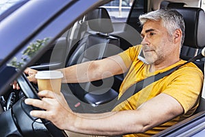 Busy Caucasian man with cupholder in arm is driving his car photo
