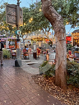 a busy city area with tables and chairs in it and a large clock in the