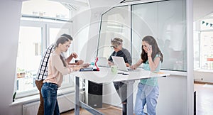 Busy co-workers using mobile technology while sharing a desk in a work hub