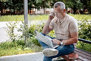 Busy, confident, successful, serious mature gray haired businessman, entrepreneur using laptop and mobile phone to call