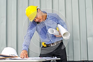 Busy construction engineer talking on phone while carrying blueprints with checking the building progress