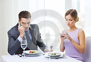 Busy couple with smartphones at restaurant