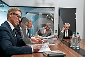 Busy day. Concentrated business people in formal wear reading some documents while having a meeting in the modern office