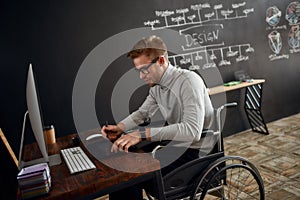 Busy designer at work. Side view of young and handsome male office worker in a wheelchair using stylus pen and digital