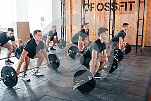 Busy by doing exercises. Group of young sportive people have crossfit day indoors in gym