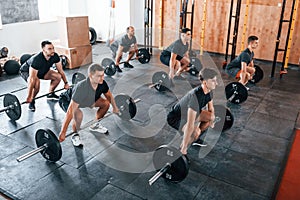 Busy by doing exercises. Group of young sportive people have crossfit day indoors in gym