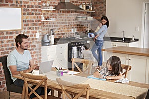 Busy Family Home With Father Working As Mother Prepares Meal