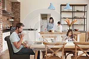 Busy Family Home With Father Working As Mother Prepares Meal