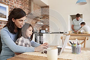 Busy Family Home With Mother Working As Father Prepares Meal