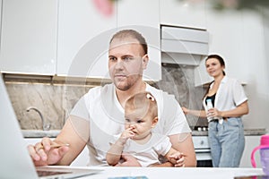 Busy father holding kid while working with laptop